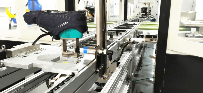 Una fotografía de aplicación en fábrica muestra el lector JT-7400 instalado junto a una fijación de transportador para el seguimiento automatizado de la producción de calzado.