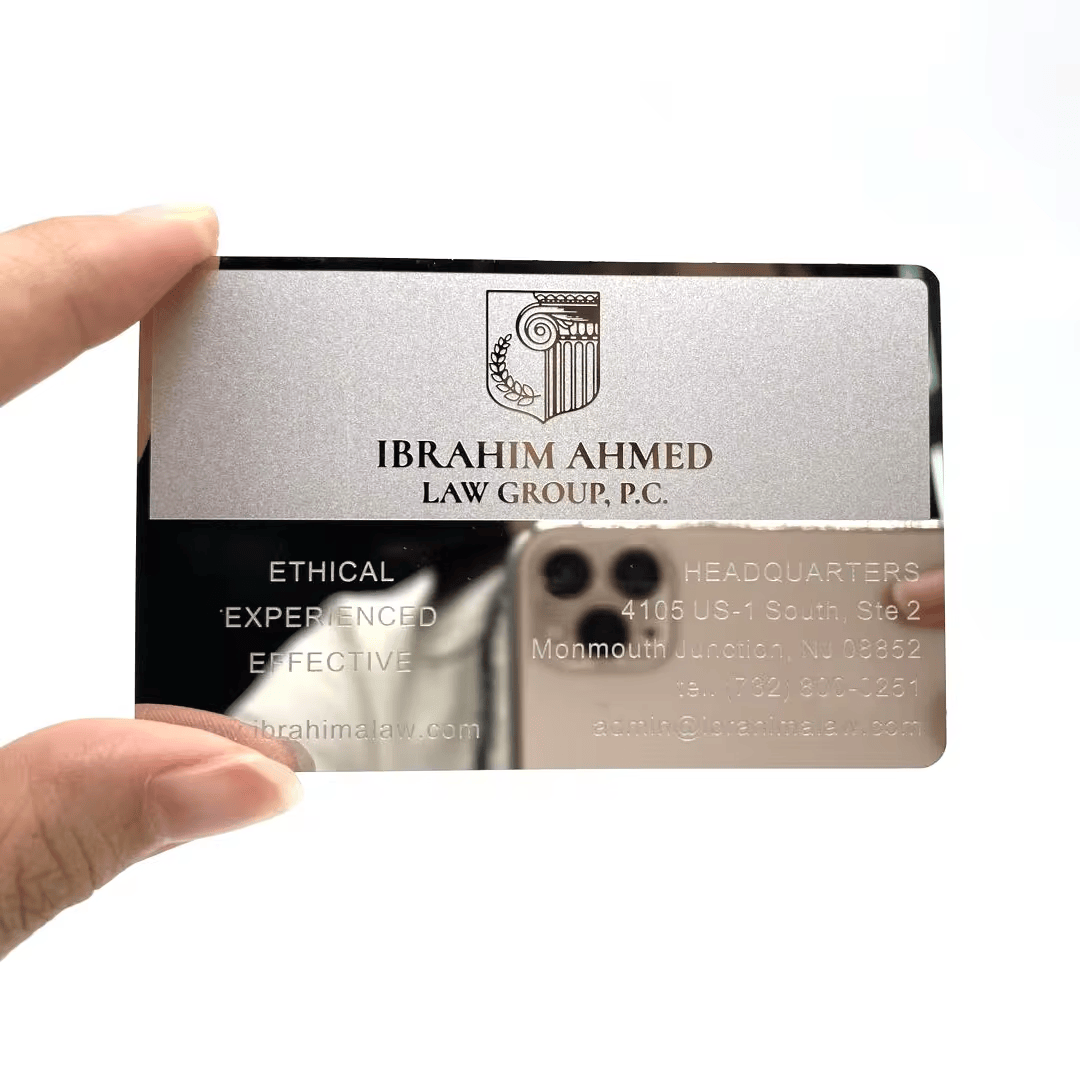 El primer plano muestra una tarjeta de presentación de metal plateado espejo con logotipo de bufete grabado y letras finas para una identidad prémium.