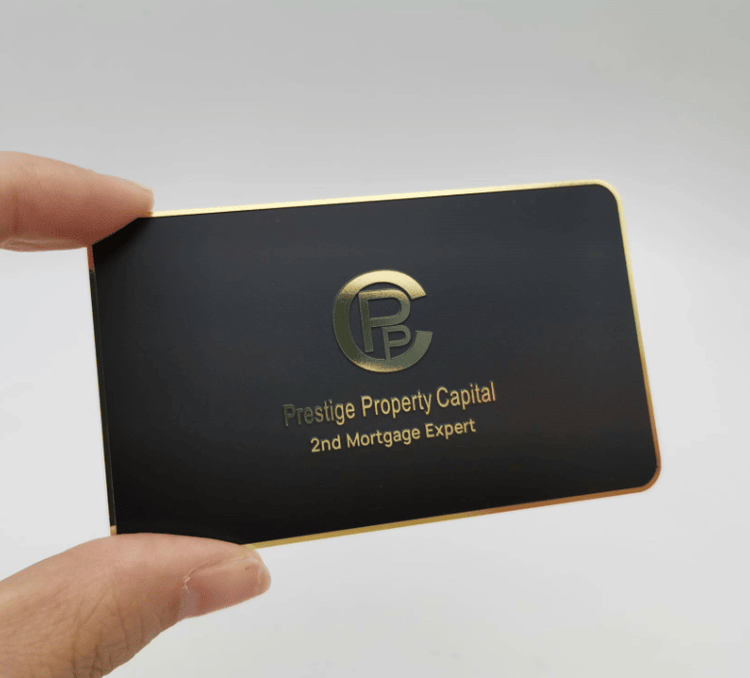 Tarjeta de visita metálica con superficie negra, bordes chapados en dorado y un logotipo en relieve centrado para marcas de lujo.