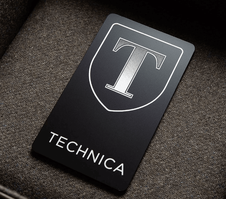 Tarjeta de visita metálica con acabado negro mate, un logotipo de escudo destacado y una imagen de marca limpia de alto contraste.
