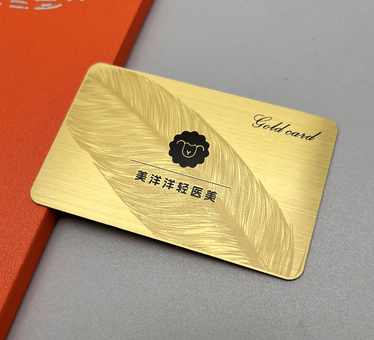 Tarjeta de visita metálica con acabado dorado cepillado y un motivo de pluma grabado para una presentación elegante de la marca.