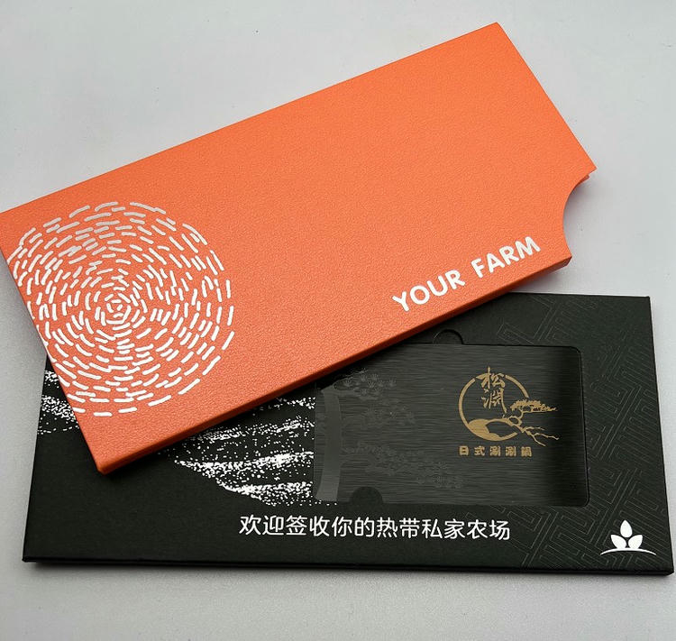 Tarjeta de visita metálica presentada en una caja naranja premium para regalos corporativos y acciones de fidelización de alto nivel.