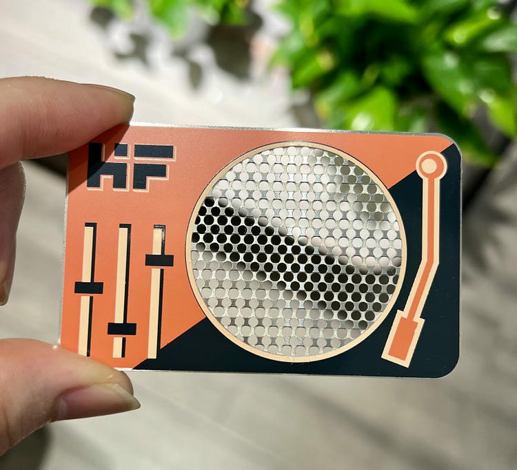 Tarjeta de visita metálica con diseño gráfico naranja y ventana circular perforada para una identificación VIP llamativa.