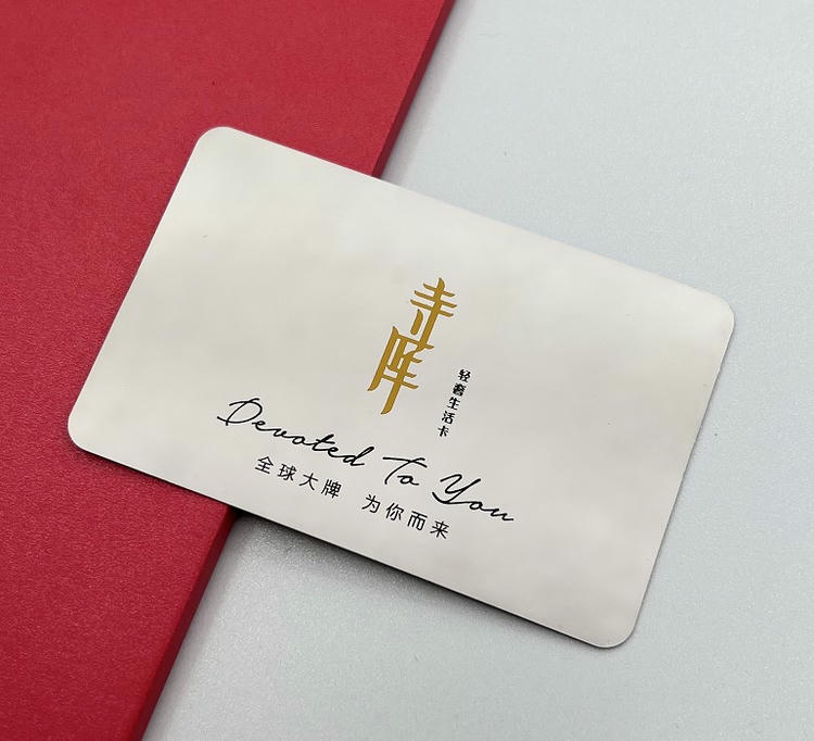Tarjeta de visita metálica con acabado blanco, letras doradas y una identidad gráfica tipo firma para miembros exclusivos.