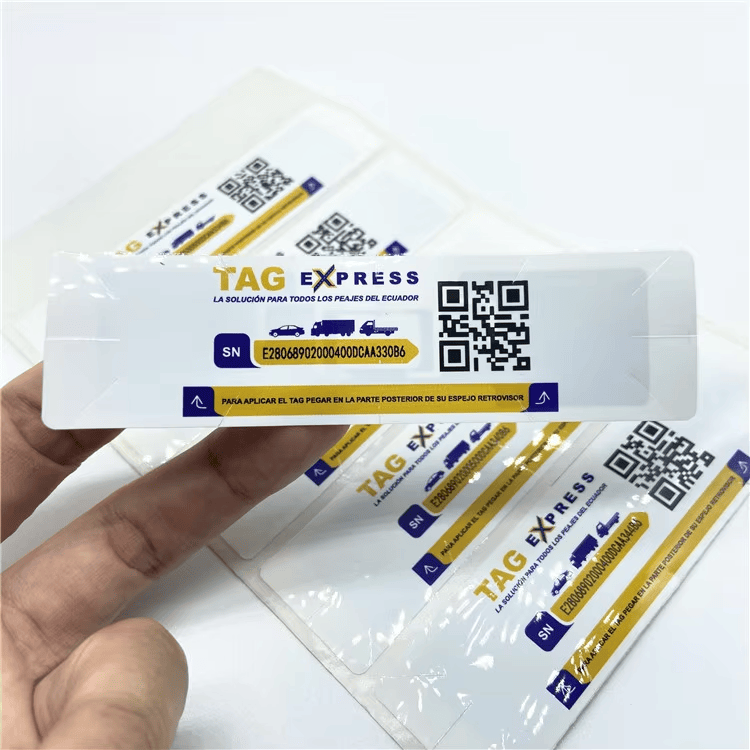 Un dedo señala una etiqueta RFID UHF para parabrisas con impresión TAG EXPRESS, código QR y espacio para el número de serie.