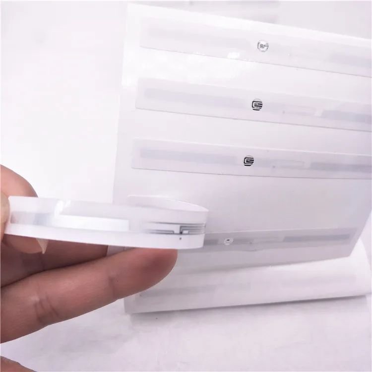Una mano dobla una etiqueta RFID LED de aviso para mostrar su perfil lateral mientras una hoja de muestras similares permanece al fondo.