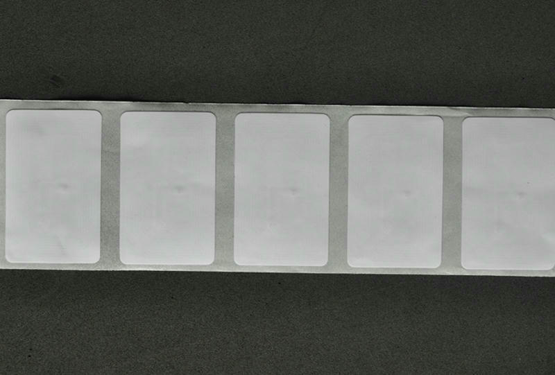 Una etiqueta RFID HF blanca se aplica a libros escolares para automatizar préstamos y mejorar el control preciso del inventario.